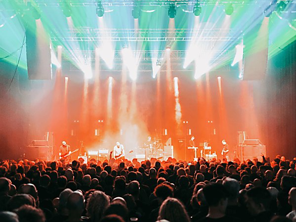 Orange and green lighting on stage at a gig with a big crowd