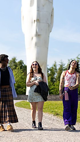 3 people walking and laughing in front of a large white sculpture