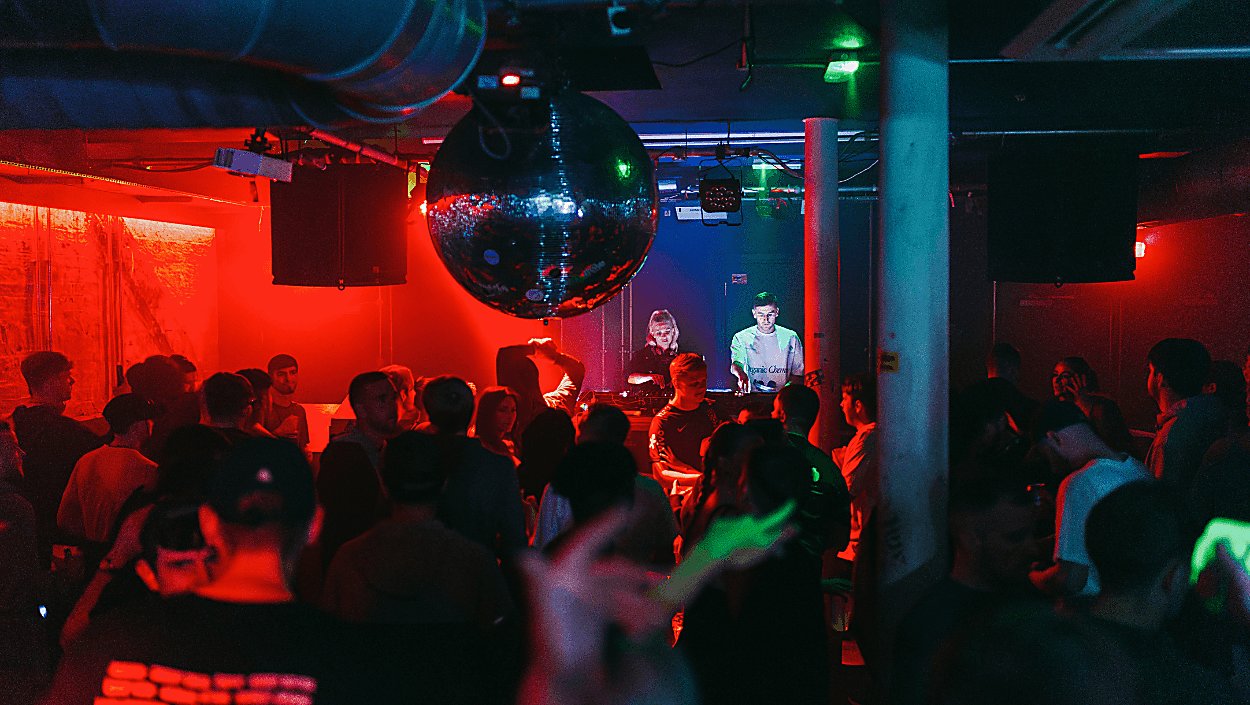 Inside a club with red lighting and a big disco ball
