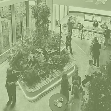 A number of people standing in a sustainable building with flowers and leaves around them. The image has a green wash over it too.