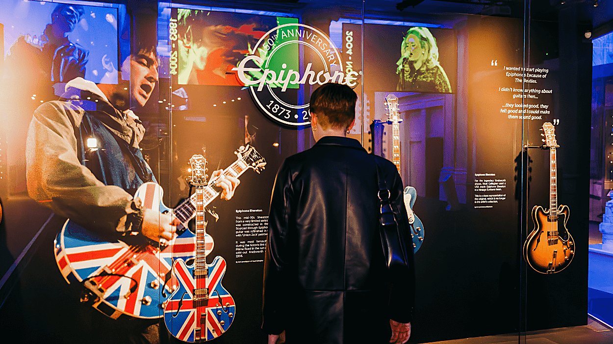 A person stood with their back to the camera looking at a display of guitars in a glass case.