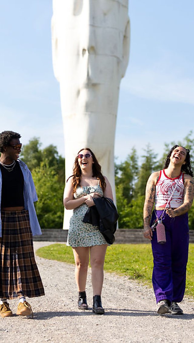 3 people walking and laughing in front of a large white sculpture