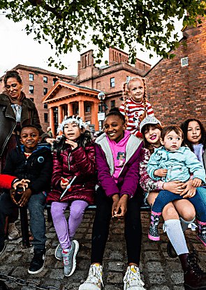 Kids and an adult sitting together at the Royal Albert Dock, smiling at the camera