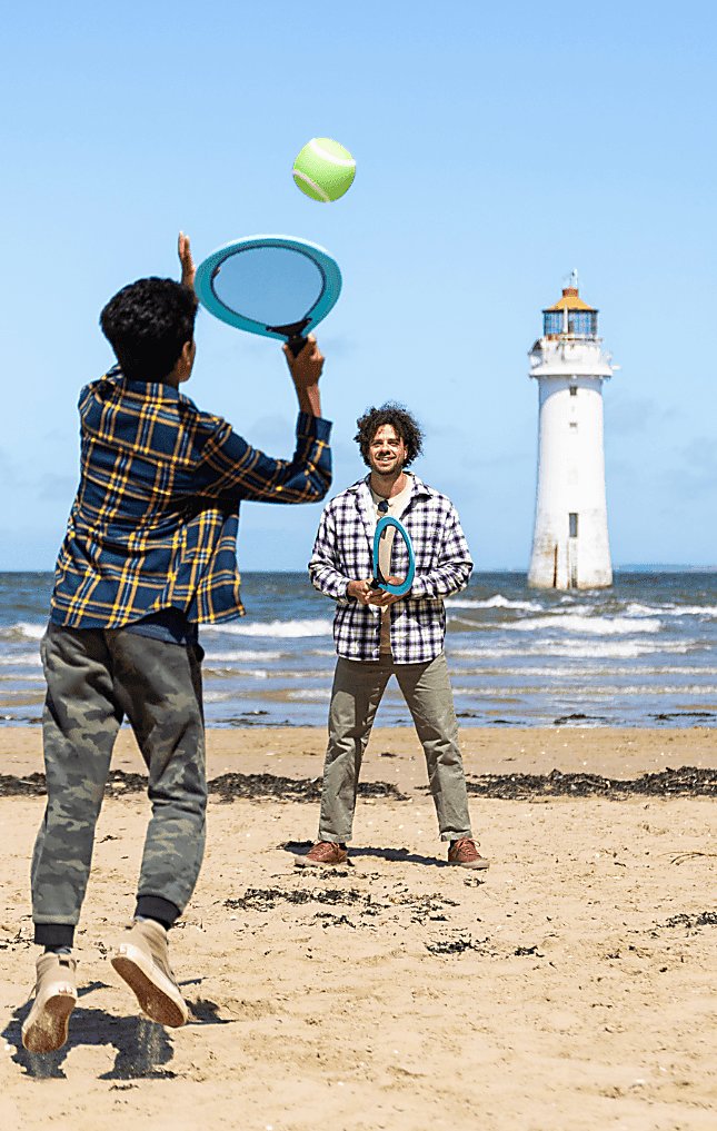 Two people playing tenning on a beach with a lighthouse in the background.
