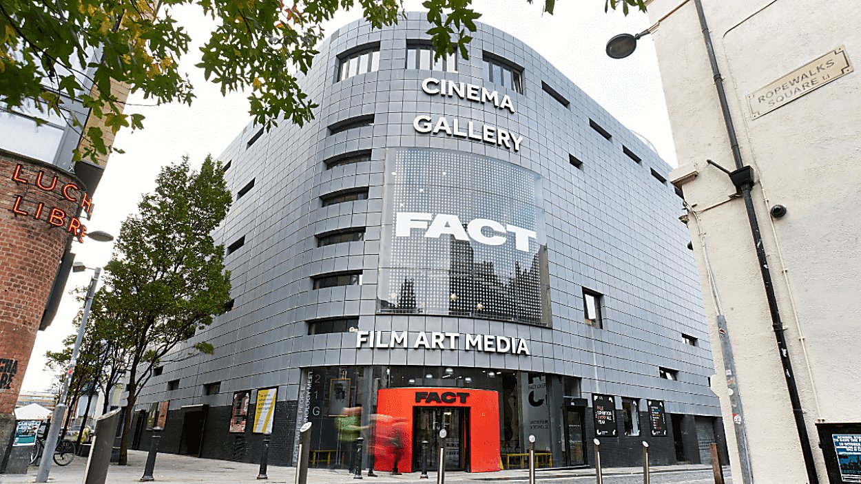 The entrance to FACT with threes lining the side of the building and a red arch leading people into the entrance of FACT.