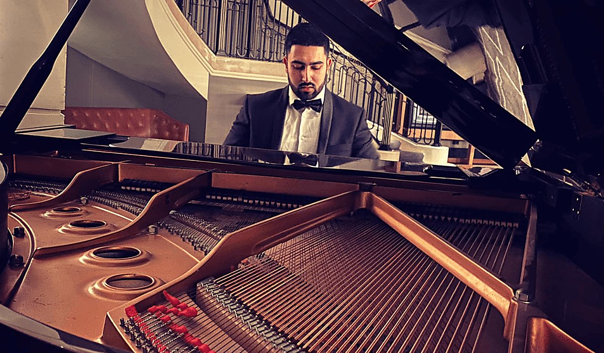 A man wearing a tuxedo sits at a grand piano which is open