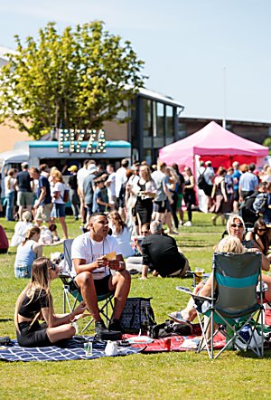 A group of people sitting on picnic blankets and chairs in a park at a food and drink festival.