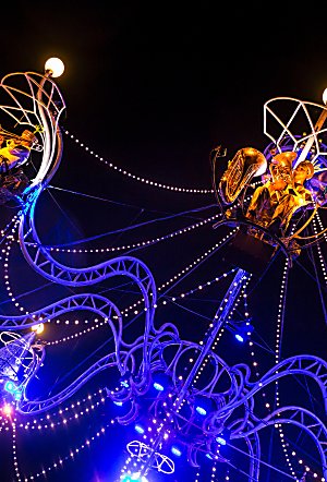 A large chandelier art piece with people sitting on it as part of a performance.