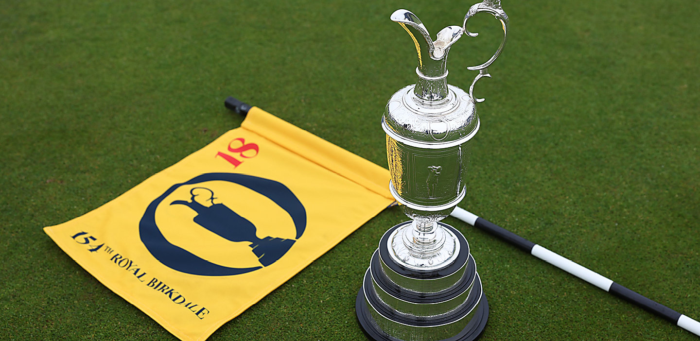 A silver trophy next to a yellow flag on the floor of some grass.