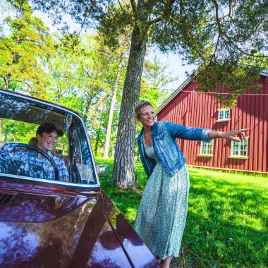 Dame peker ut veien for en bil som kommer forbi på bygdetunet