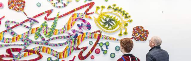 Two guests view a large, colorful abstract artwork displayed on a white wall inside First Financial Center.