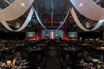 Ceiling Drapery Hanging Down in Front of an Event Stage and Decorated Round Banquet Tables