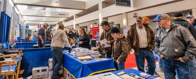 Convention center concourse with attendees conversing at trade show vendor booths along the entire hallway