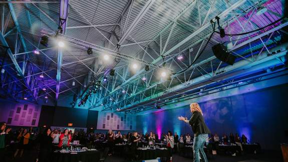 Exhibit Hall Conference Speaker Standing on Stage in front of Seated Attendees