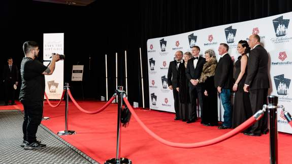 A group of people posing in front of a backdrop for a photo at a red carpet gala event