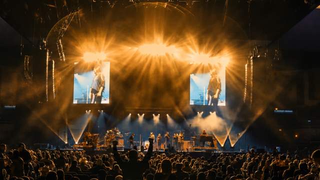Crowd gathered inside the Sudduth Coliseum within the Lake Charles Event Center during a live concert with dramatic golden stage lighting, large video screens, and an energetic arena atmosphere.