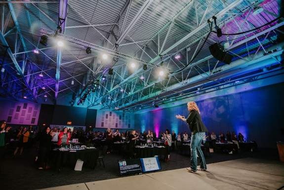 Exhibit Hall Conference Speaker Standing on Stage in front of Seated Attendees