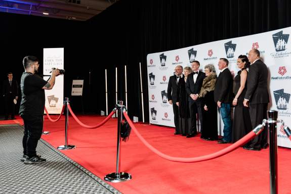 A group of people posing in front of a backdrop for a photo at a red carpet gala event