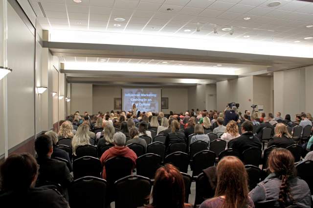 Meeting room with attendees watching a speaker and their projected presentation