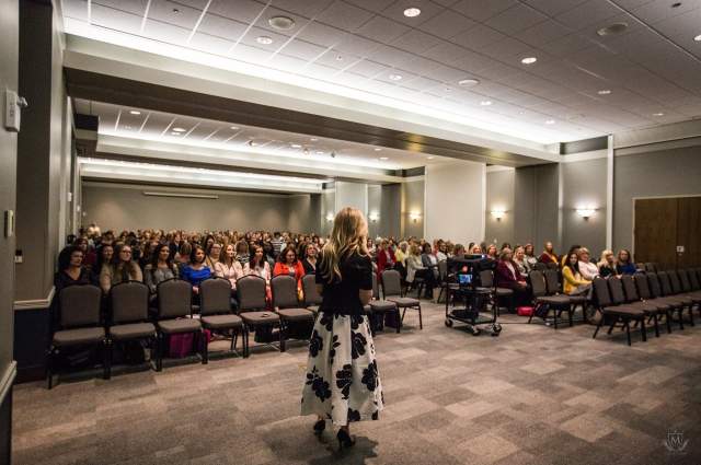 Female Presenter Facing Room of Attendees During Conference