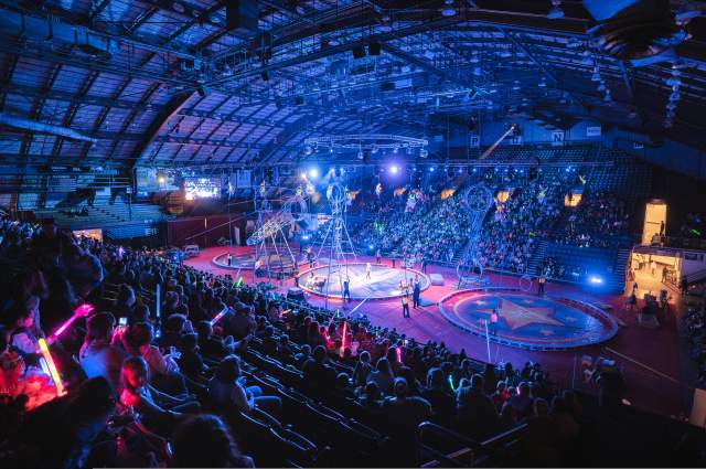 Fans viewing a Shrine Circus performance with aerial performers on the arena floor