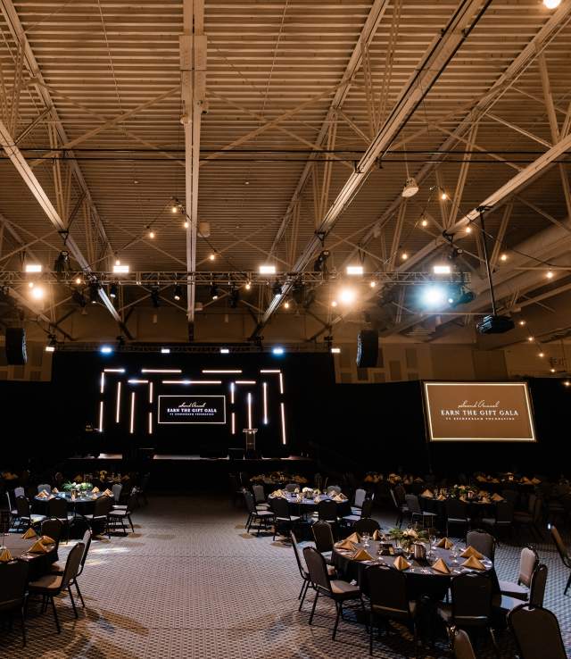 Large Exhibit Hall Set Up for Earn the Gift Gala with Stage and Round Guest Tables