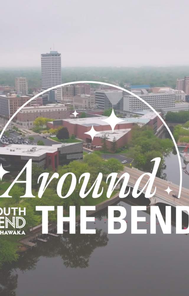Aerial view of South Bend, Indiana, showcasing skyline, green parks, and rivers with text overlay: "Around the Bend."