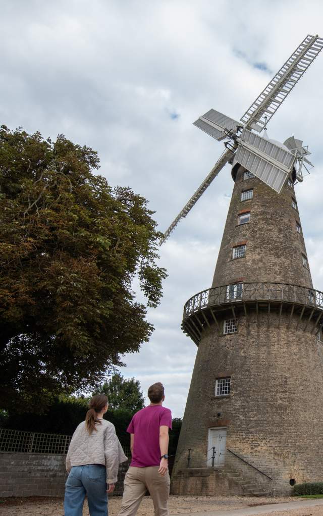 two people walking towards a windmill in the countryside