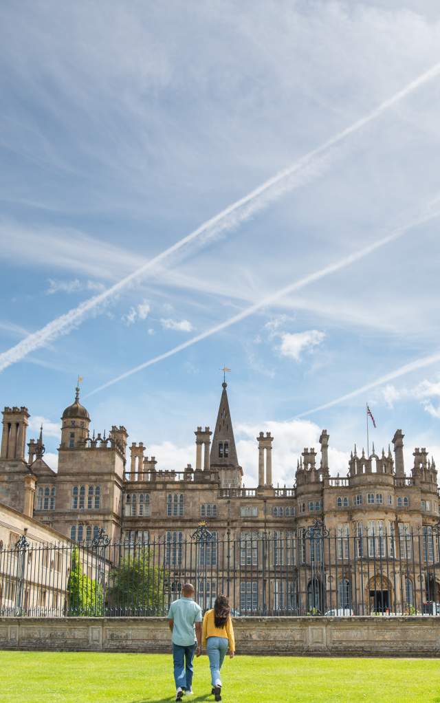 A sunny day exterior of Burghley House near Stamford with two people walking towards the gates
