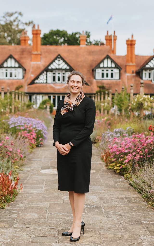 An image of the Petwood Hotel taken from the gardens with a woman stood on a path looking at the camera