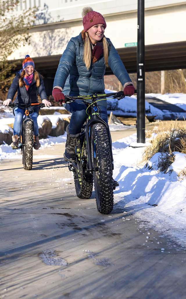 two girls on fat tire bikes on a sidewalk surrounded by snow