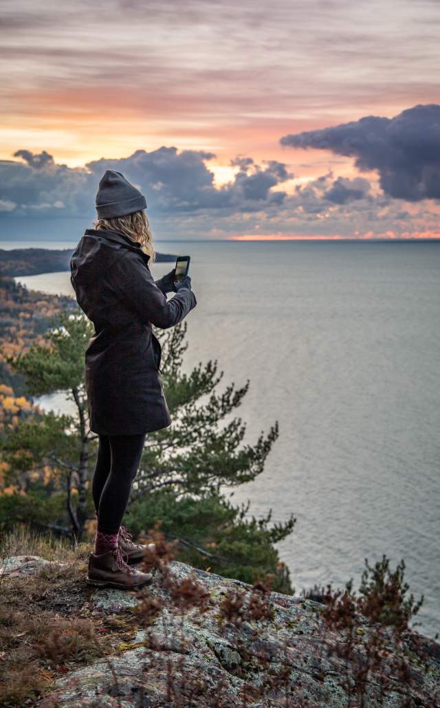 A hiker taking a photograph on a hike at Bare Bluff at sunrise, located in Michigan's Upper Peninsula, USA