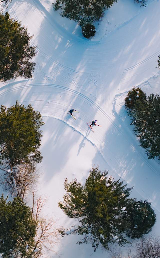 aerial view of two cross country skiiers on a wooded snow covered trail