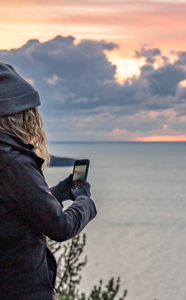 A hiker taking a photograph on a hike at Bare Bluff at sunrise, located in Michigan's Upper Peninsula, USA