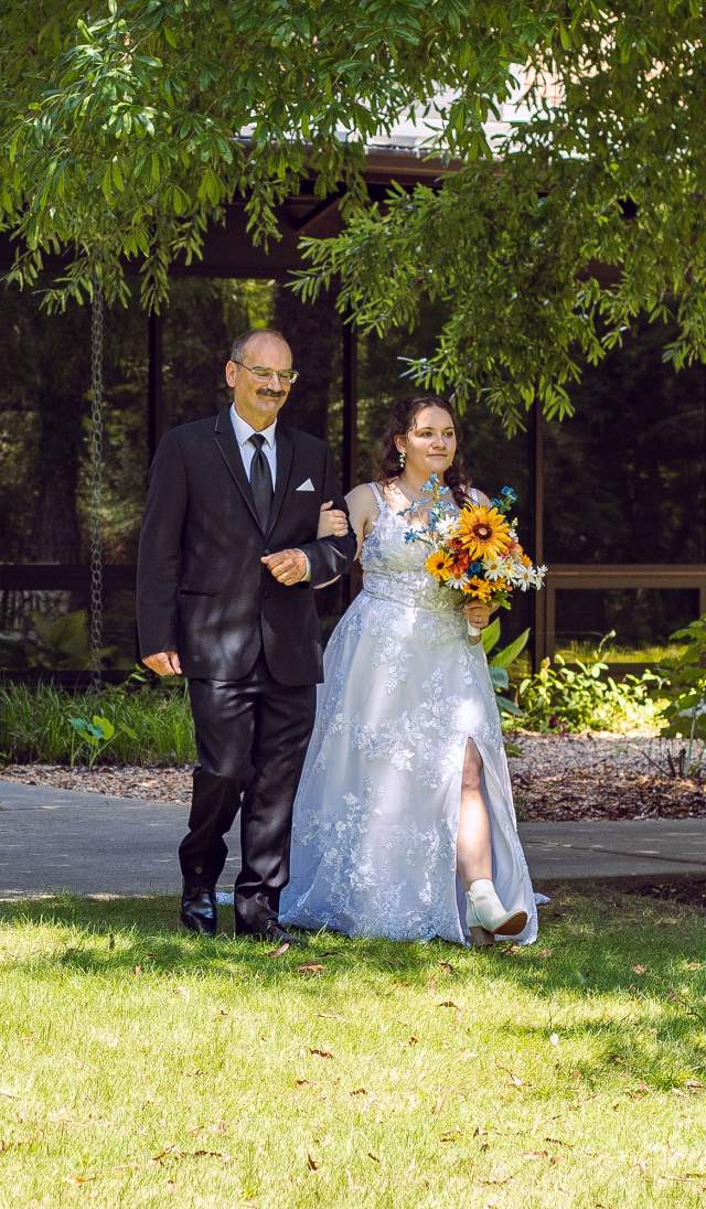 Bride walking down an outdoor aisle at Cape Fear Botanical Garden in Fayetteville, NC, during a garden wedding ceremony.