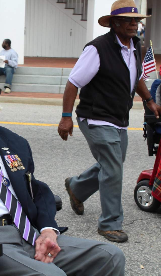 An older adult using a motorized wheelchair participates in a community event alongside others, highlighting accessible routes and mobility support in a public setting.