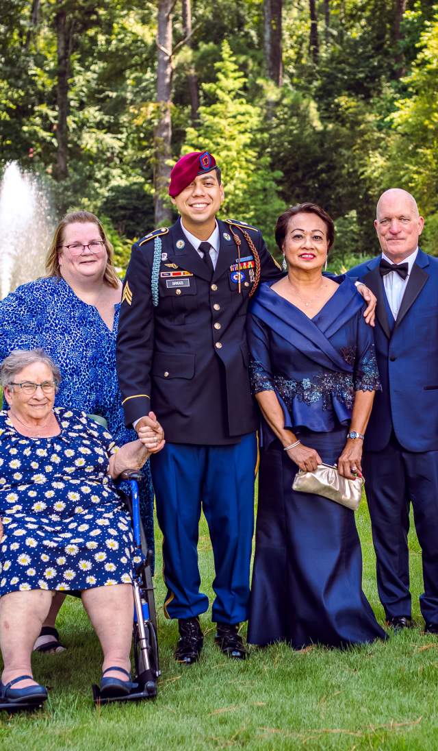 Multigenerational family portrait at a Cape Fear Botanical Gardens outdoor wedding in Fayetteville, NC, featuring a U.S. Army service member in dress uniform and family, gathered in a garden setting.