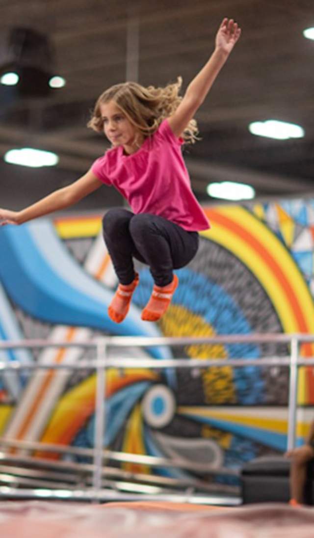 A young girl jumping on a trampoline while her friends sit nearby