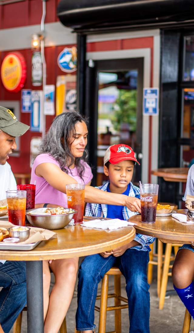 Family and friends gathered around an outdoor restaurant table sharing food and drinks together