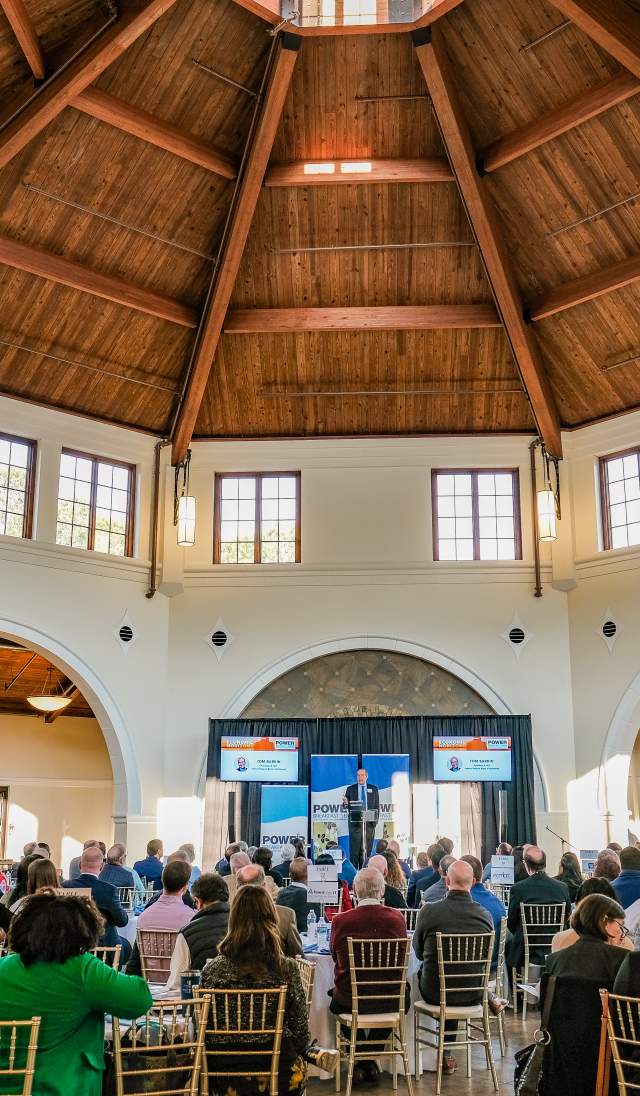 Conference attendees seated inside the Cape Fear Botanical Garden event hall in Fayetteville, NC, listening to a speaker under the vaulted wooden ceiling.