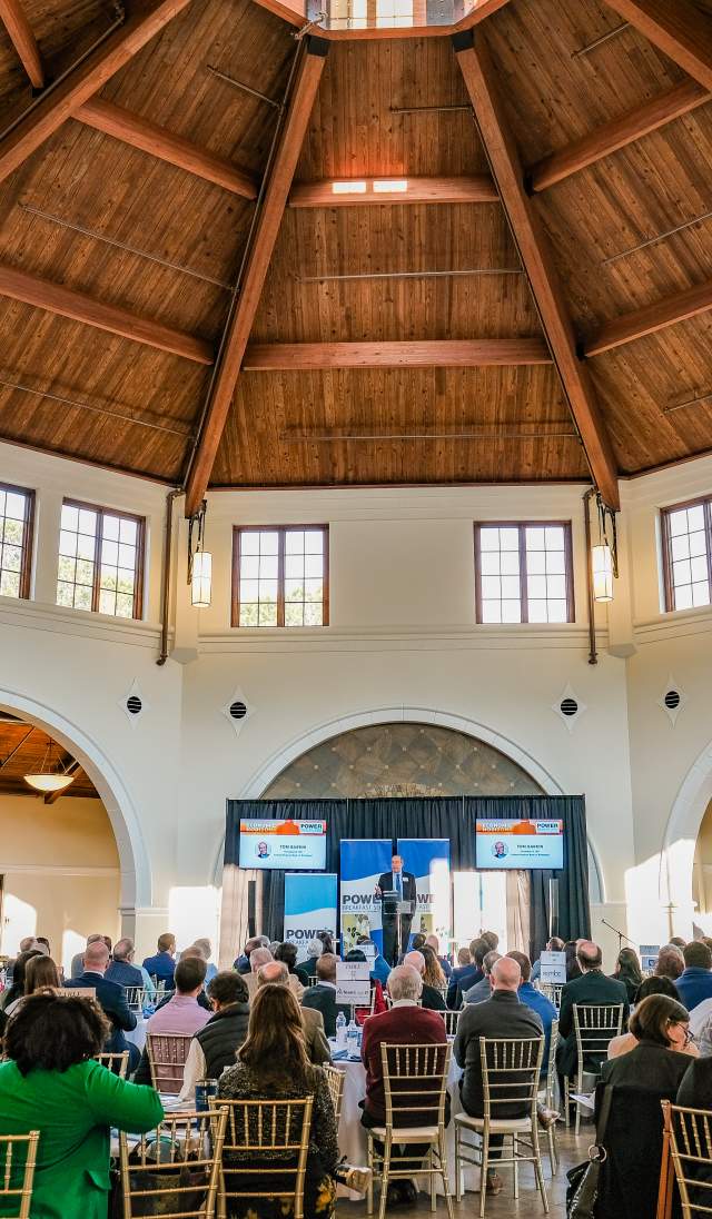 Conference attendees seated inside the Cape Fear Botanical Garden event hall in Fayetteville, NC, listening to a speaker under the vaulted wooden ceiling.