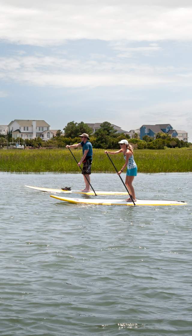a couple paddleboarding in the marsh