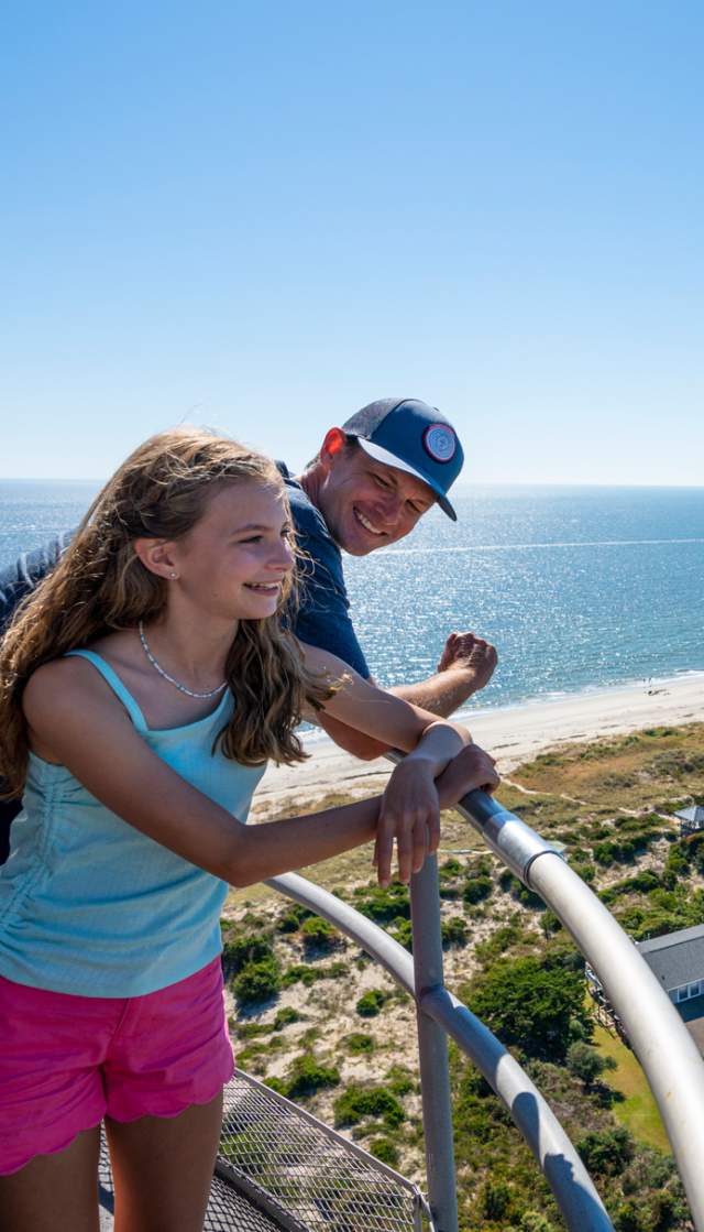 a father and daughter overlooking Caswell Beach from the top of the Oak Island Lighthouse