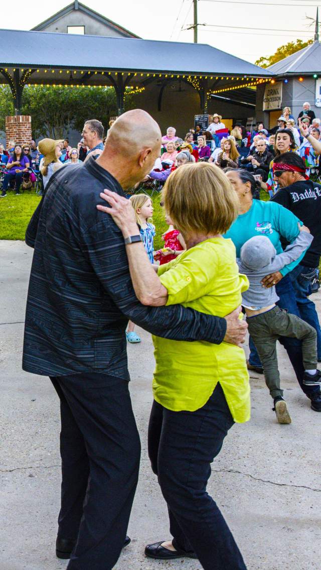 People of all ages dance near the stage during a Mandeville Live! free Friday concert at the Mandeville Trailhead, with a crowd gathered under the pavilion and on the lawn.