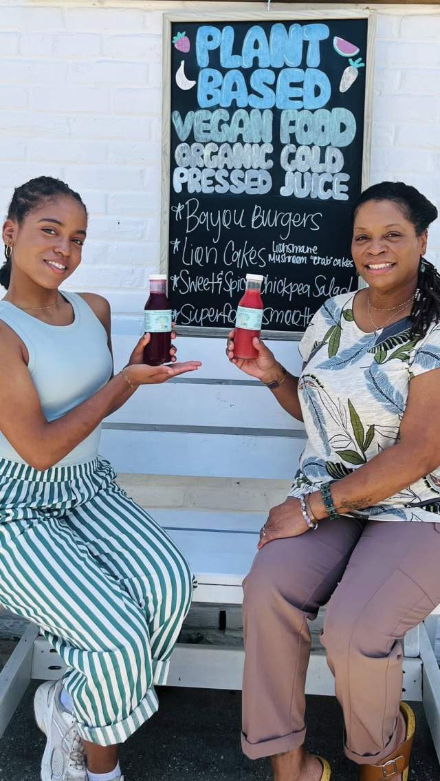Alicia and Carmen Norman of The Earthly Elephant display their bottled juices, seated outdoors on a bench.