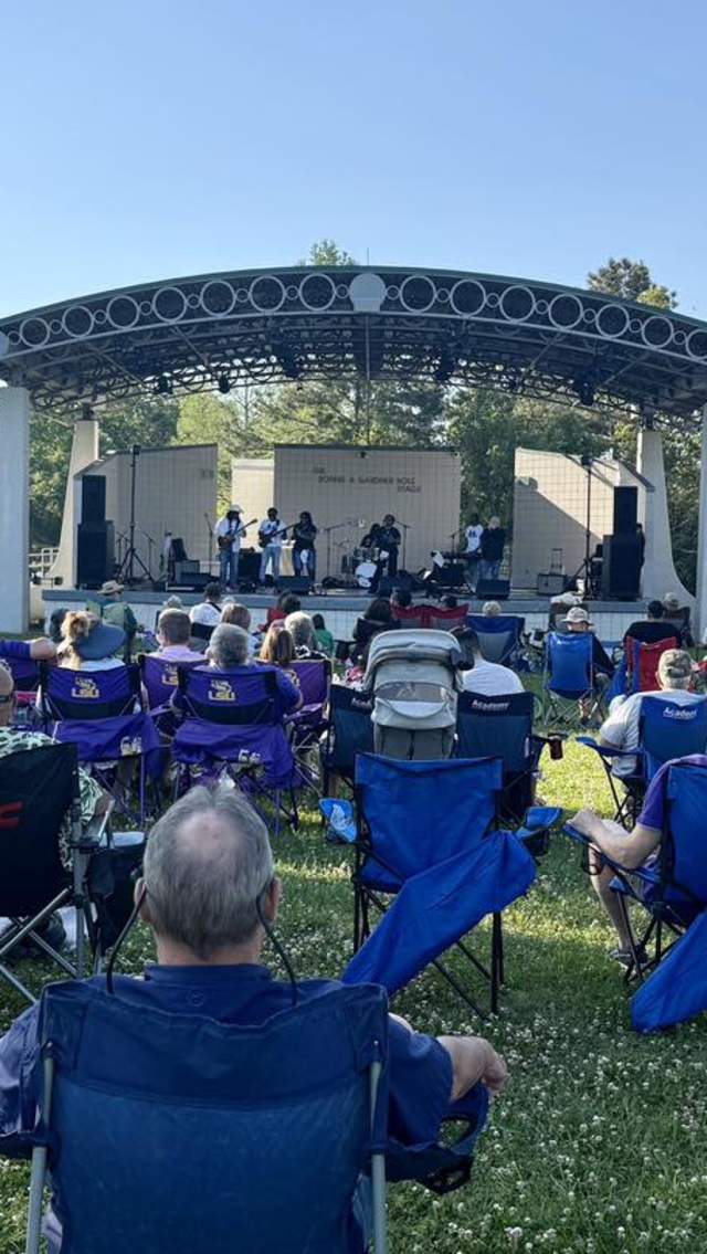 Crowd seated in lawn chairs on the grass at a Bayou Jam concert, watching Soul Revival perform on the outdoor amphitheater stage on a sunny afternoon.