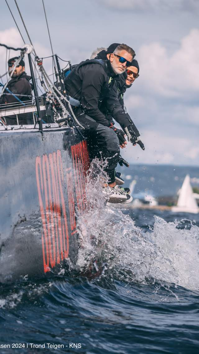 Menn som sitter på kanten av en seilbåt i full fart
