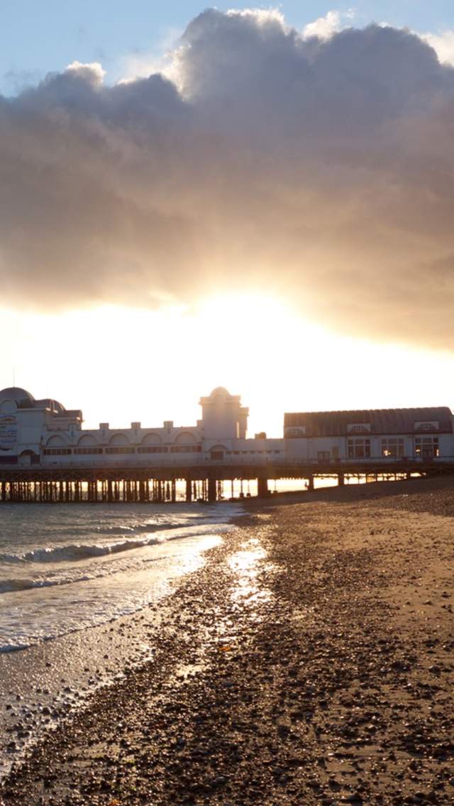 The sun sets behind South Parade Pier, with Southsea beach and sea in the foreground