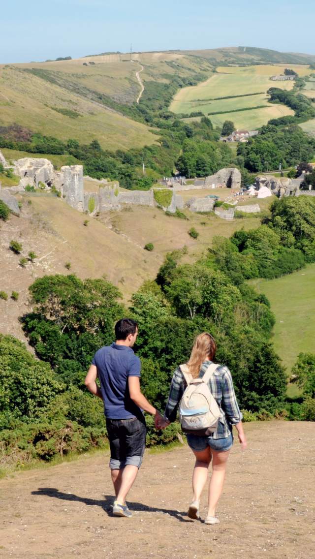 Couple walking down a hill to Corfe Castle Village in Dorset with the Castle in the background