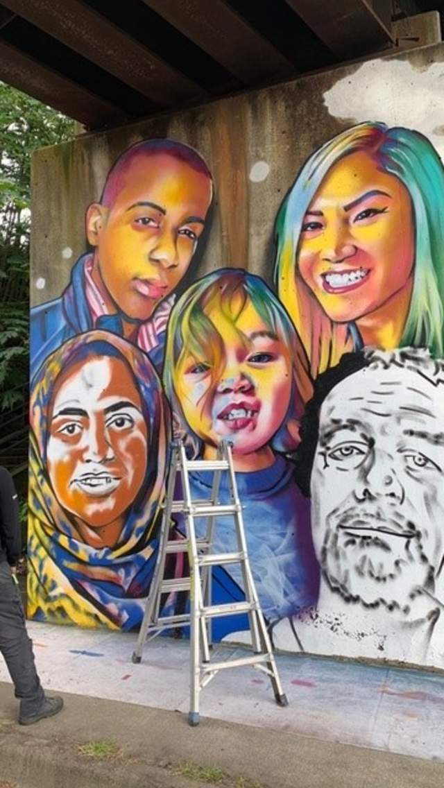 Artist and ladder in front of a wall mural under a bridge